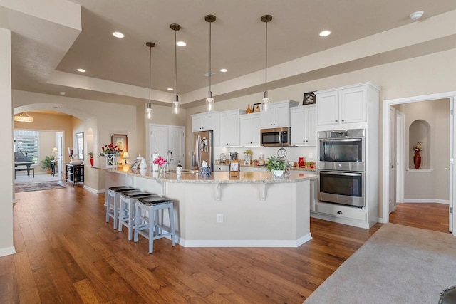 kitchen featuring arched walkways, appliances with stainless steel finishes, a kitchen breakfast bar, and wood finished floors