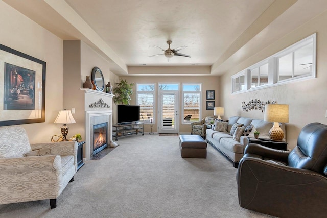 carpeted living room featuring a ceiling fan, a tray ceiling, and a tiled fireplace