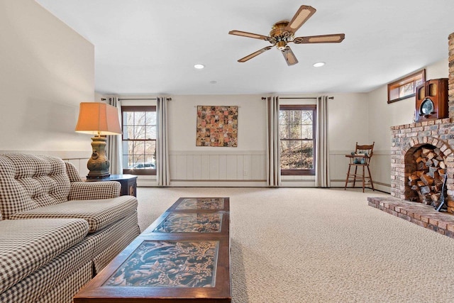 carpeted living area with a wainscoted wall, a ceiling fan, recessed lighting, and a brick fireplace