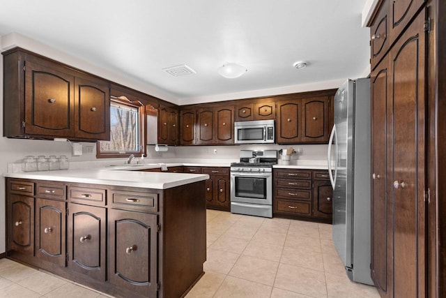 kitchen with dark brown cabinetry, light tile patterned floors, light countertops, a peninsula, and stainless steel appliances