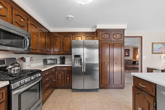 kitchen featuring light countertops, appliances with stainless steel finishes, light tile patterned floors, and dark brown cabinetry