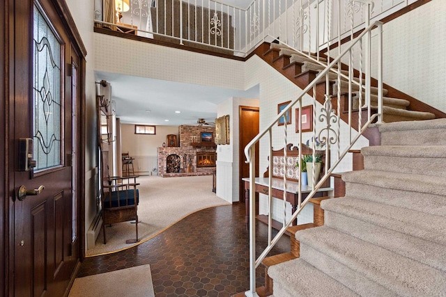 foyer featuring stairs, a towering ceiling, a fireplace, and wallpapered walls