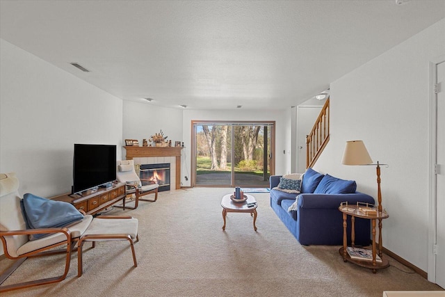 living area featuring visible vents, carpet flooring, stairs, and a tile fireplace