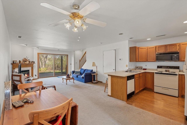 kitchen featuring a sink, a peninsula, open floor plan, light carpet, and white appliances