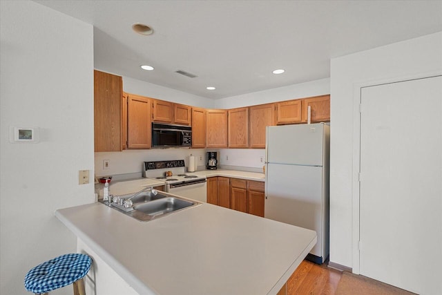 kitchen featuring a sink, white appliances, light countertops, a peninsula, and recessed lighting