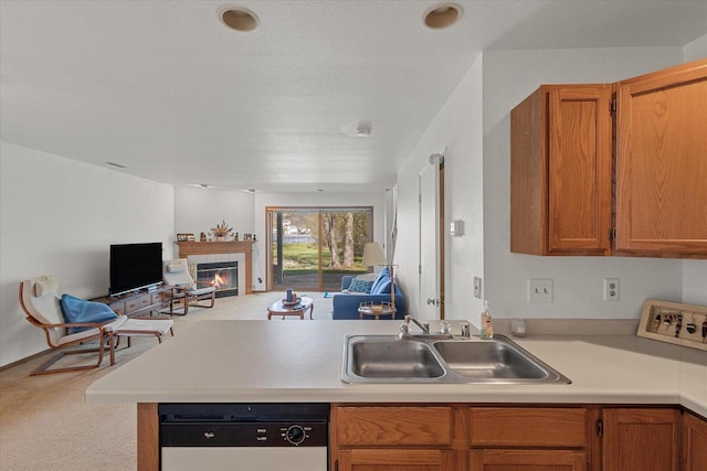 kitchen with a peninsula, open floor plan, a tiled fireplace, a sink, and dishwasher