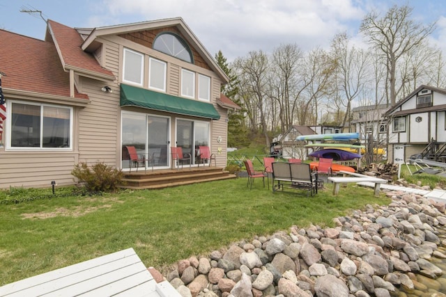 rear view of house with a lawn, a deck, and roof with shingles