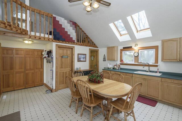 dining space with a ceiling fan, light floors, and vaulted ceiling with skylight