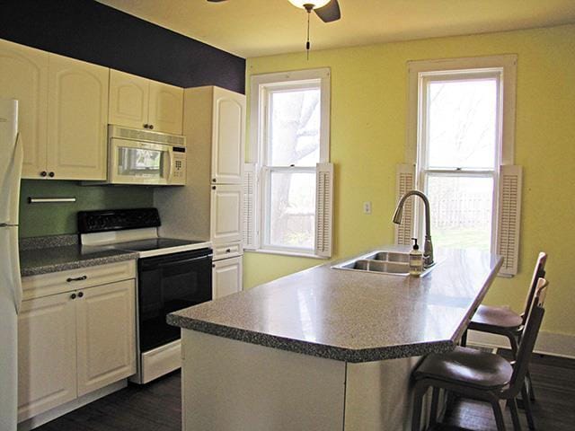 kitchen with a sink, white microwave, electric stove, a breakfast bar, and dark wood-type flooring