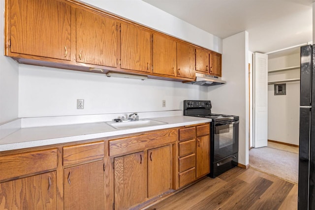 kitchen with black range with electric stovetop, wood finished floors, a sink, light countertops, and under cabinet range hood