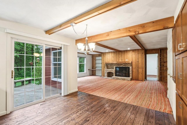 S9073 Timbercrest Trl, Prairie Du Sac, WI 53578 - unfurnished living room with beam ceiling, dark wood-style floors, a chandelier, wood walls, and a brick fireplace