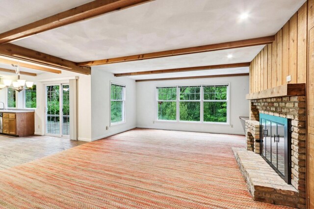 S9073 Timbercrest Trl, Prairie Du Sac, WI 53578 - unfurnished living room with a brick fireplace, beam ceiling, baseboards, a chandelier, and light colored carpet