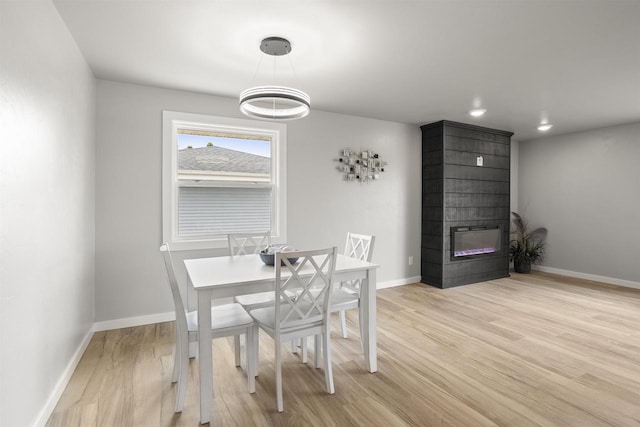dining room with light wood-style floors, a large fireplace, and baseboards