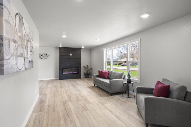 living area featuring recessed lighting, baseboards, a large fireplace, and light wood-style flooring