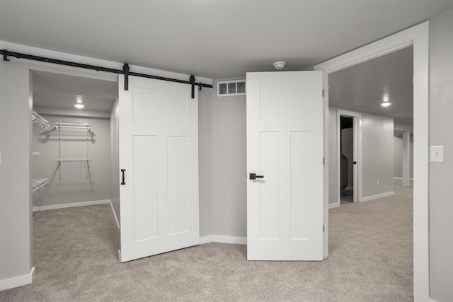 basement with visible vents, a barn door, baseboards, and light carpet