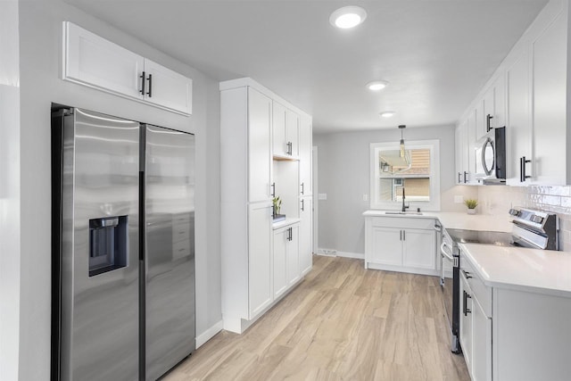 kitchen with white cabinetry, light countertops, baseboards, stainless steel appliances, and light wood-style flooring