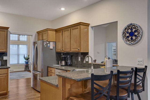 kitchen featuring wood finished floors, a kitchen bar, tasteful backsplash, a sink, and stainless steel appliances