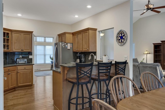 kitchen featuring ceiling fan, backsplash, wood finished floors, freestanding refrigerator, and a breakfast bar