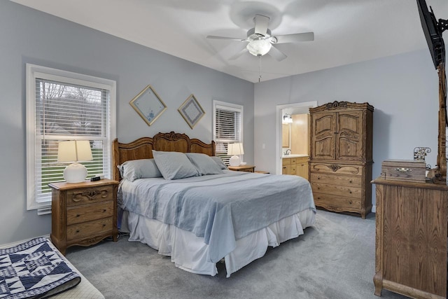 bedroom with light colored carpet, a ceiling fan, and ensuite bath