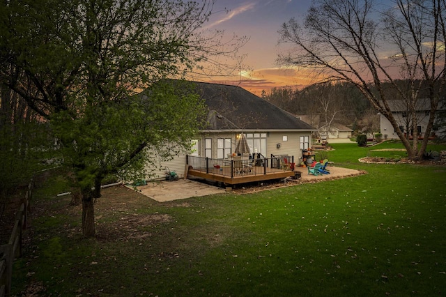 back of house at dusk with a lawn and a deck