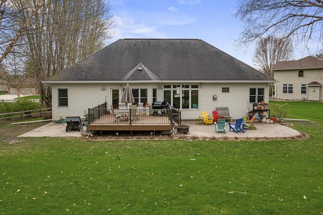 back of property featuring a lawn, a deck, a patio area, an outdoor fire pit, and a shingled roof