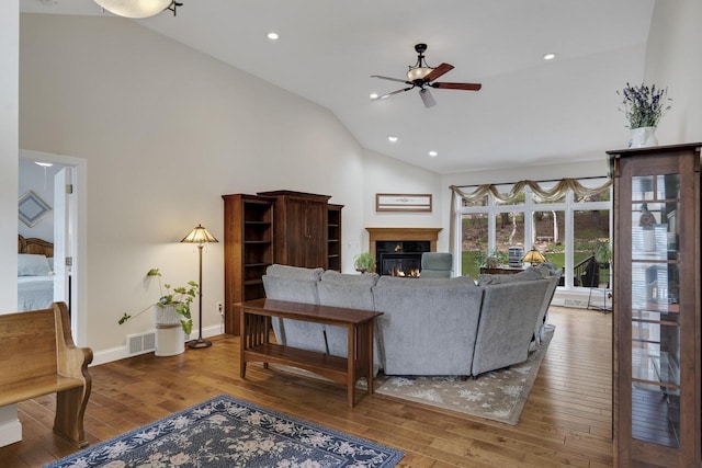 living room featuring visible vents, a glass covered fireplace, ceiling fan, high vaulted ceiling, and hardwood / wood-style flooring