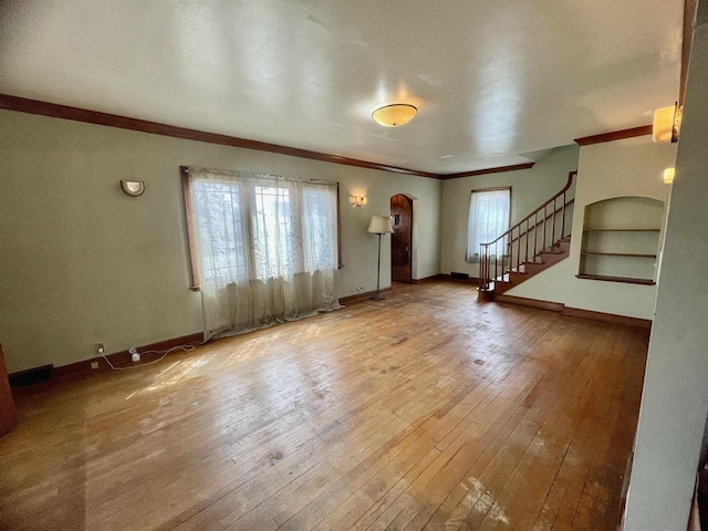 227 1st St, Baraboo, WI 53913 - unfurnished living room featuring crown molding, arched walkways, a wealth of natural light, and hardwood / wood-style flooring
