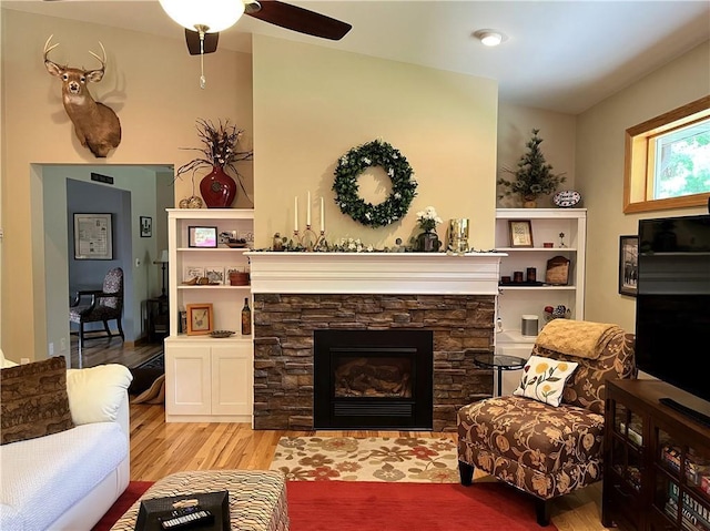 living room featuring ceiling fan, a fireplace, and wood finished floors