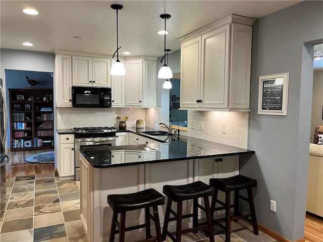 kitchen featuring a peninsula, black microwave, dark countertops, stainless steel gas range oven, and a sink