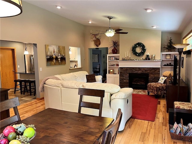 living area with a stone fireplace, light wood-style flooring, a ceiling fan, recessed lighting, and vaulted ceiling