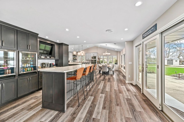 kitchen with a breakfast bar area, wine cooler, vaulted ceiling, and light wood-type flooring