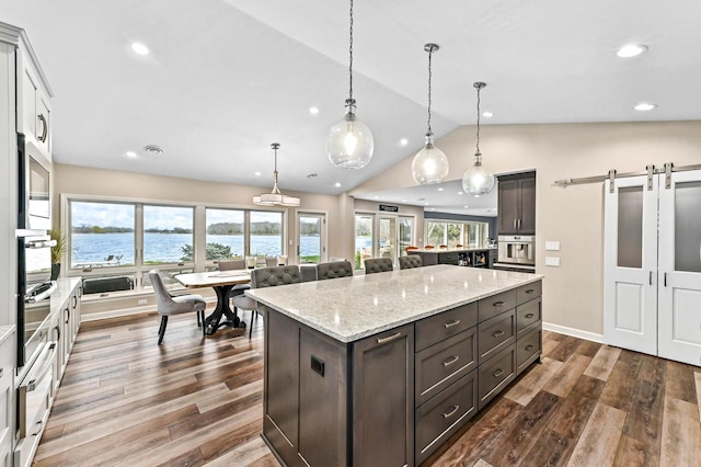 kitchen featuring a kitchen island, a barn door, a water view, dark wood finished floors, and vaulted ceiling