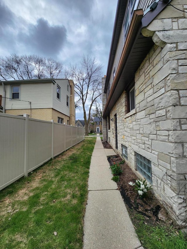 view of side of home featuring fence and stone siding