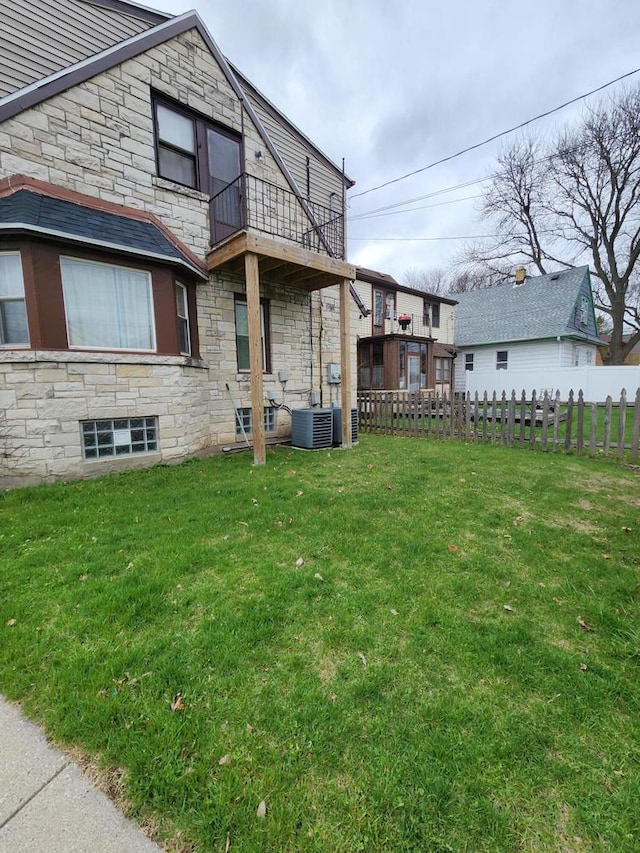 back of property with fence, a yard, a balcony, and stone siding