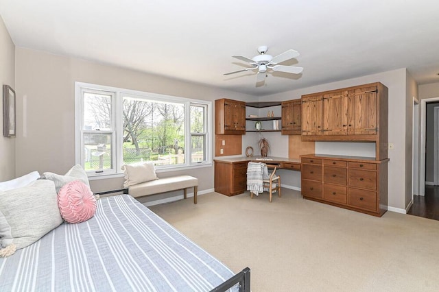 bedroom with a ceiling fan, baseboards, light colored carpet, and built in desk