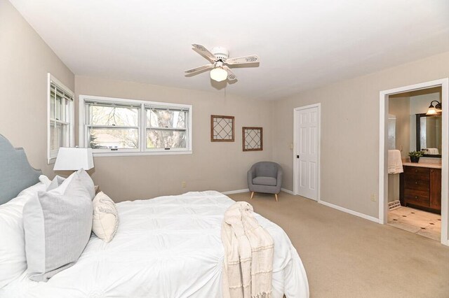 bedroom featuring baseboards, ceiling fan, ensuite bath, and light colored carpet