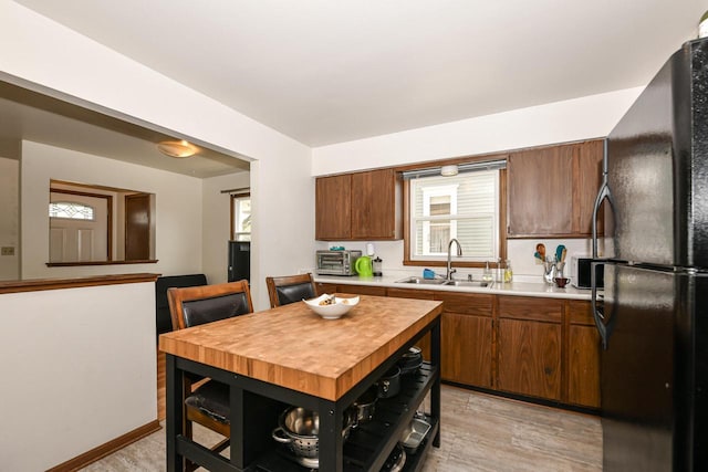 kitchen with open shelves, a sink, light wood finished floors, light countertops, and freestanding refrigerator