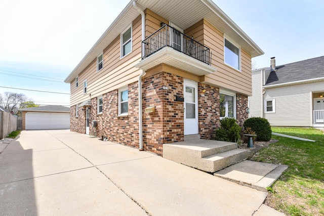 view of front of property with a detached garage, an outdoor structure, brick siding, and a balcony