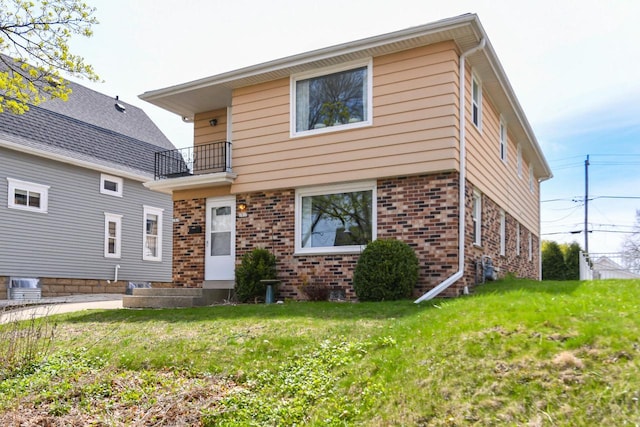 view of front of home featuring brick siding, a balcony, and a front lawn