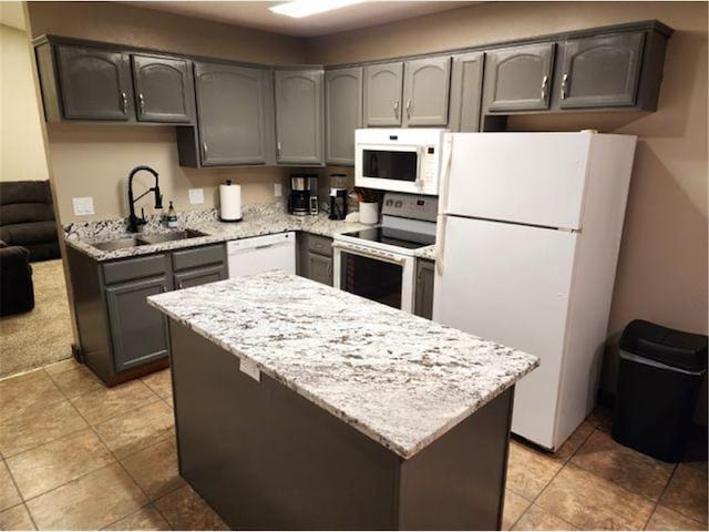 kitchen featuring light stone counters, a sink, white appliances, gray cabinets, and a center island