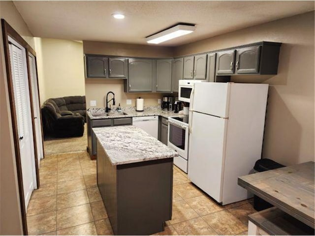 kitchen with gray cabinetry, a sink, a kitchen island, and white appliances
