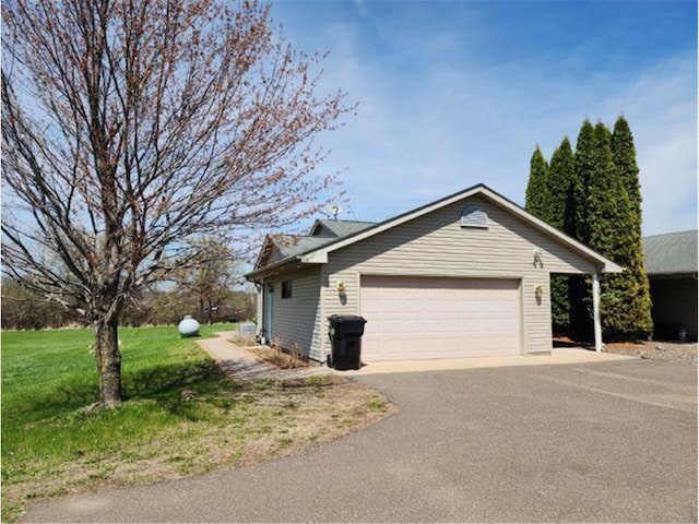 view of side of property with an attached garage, a yard, and aphalt driveway