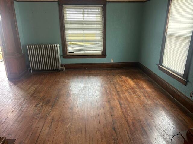 unfurnished room featuring wood-type flooring, baseboards, radiator heating unit, and a healthy amount of sunlight