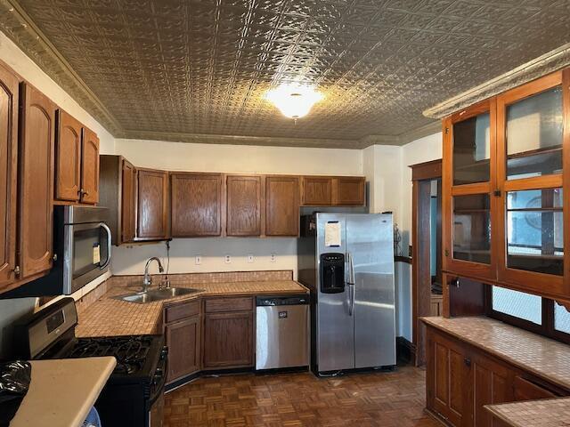 kitchen featuring a sink, appliances with stainless steel finishes, an ornate ceiling, and glass insert cabinets