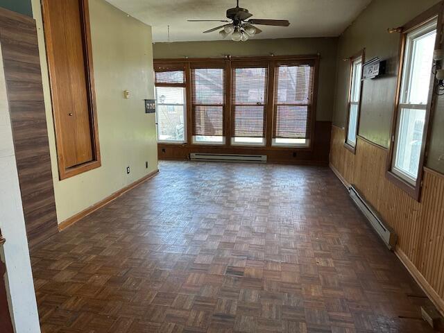 unfurnished room featuring ceiling fan, wood walls, baseboards, a baseboard radiator, and a baseboard heating unit