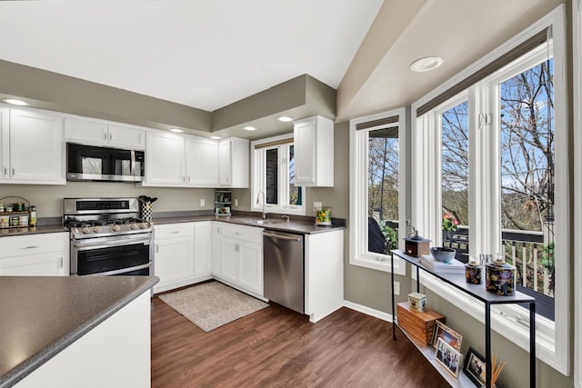 kitchen featuring dark countertops, dark wood-style floors, white cabinets, a sink, and appliances with stainless steel finishes