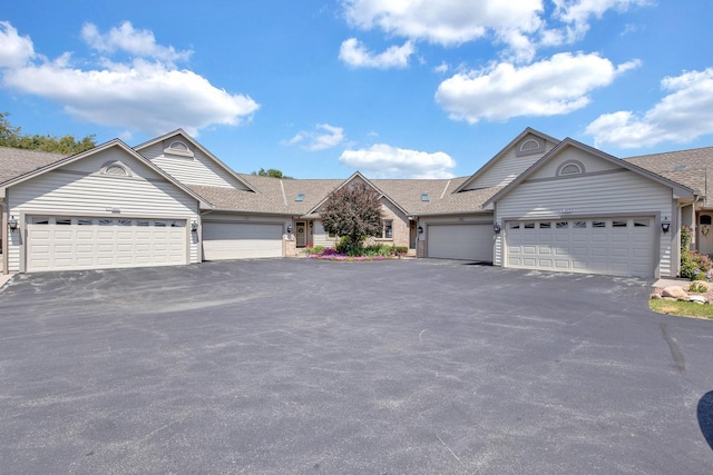 ranch-style home with an attached garage, a shingled roof, and aphalt driveway