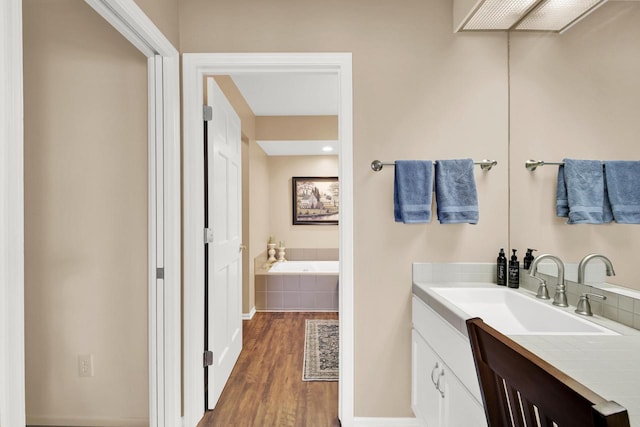 full bath with vanity, baseboards, a garden tub, and wood finished floors