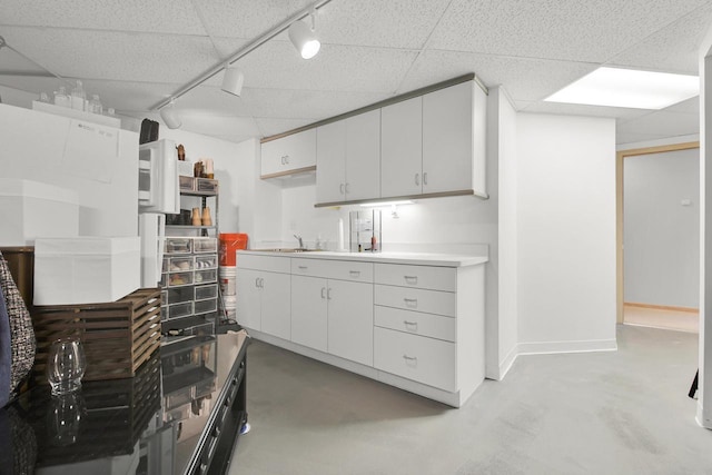 kitchen featuring light countertops, concrete flooring, a drop ceiling, and a sink