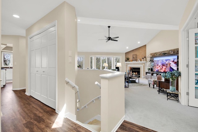 stairway featuring wood finished floors, lofted ceiling, a warm lit fireplace, recessed lighting, and a ceiling fan